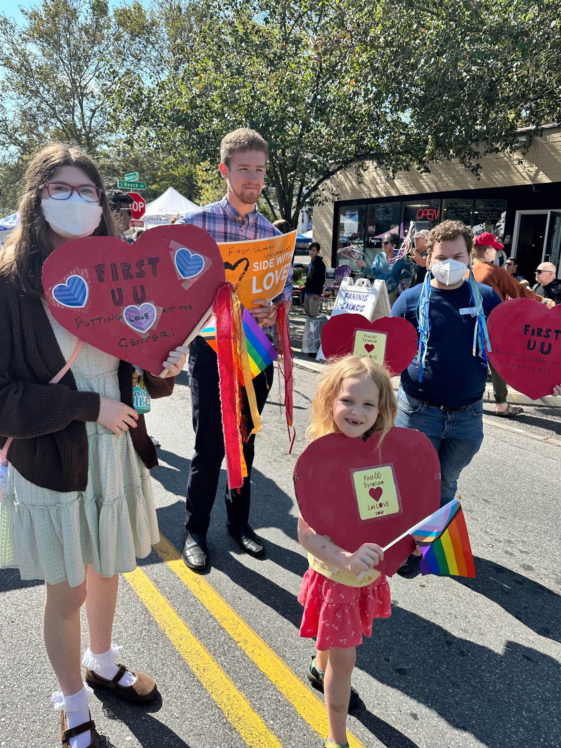 A small group of young people march in a parade while carrying hearts and signs.