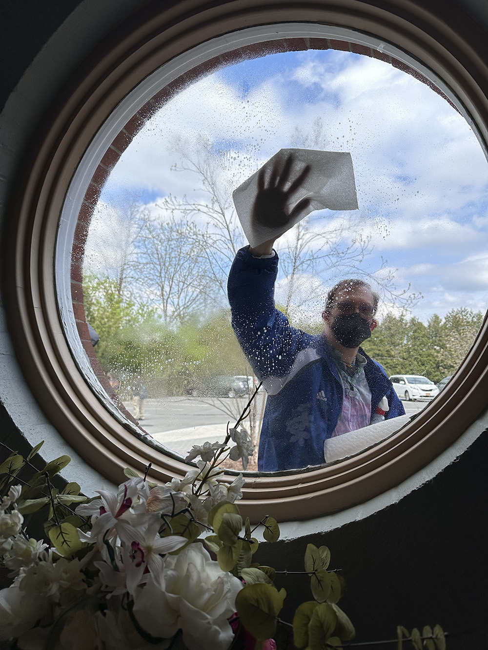 A masked person wipes the outside of a round window.
