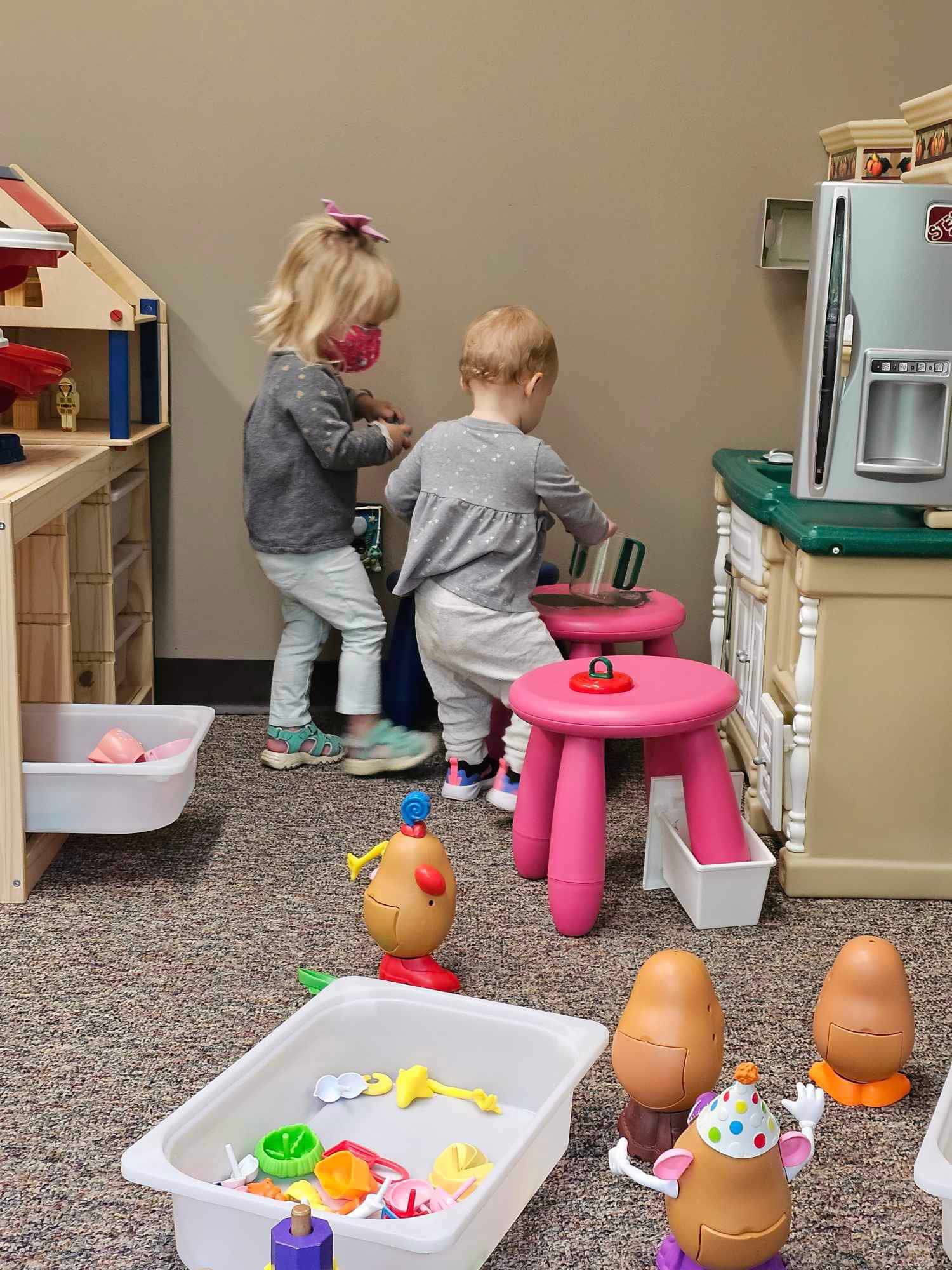 Two toddlers play with food items in a play kitchen.
